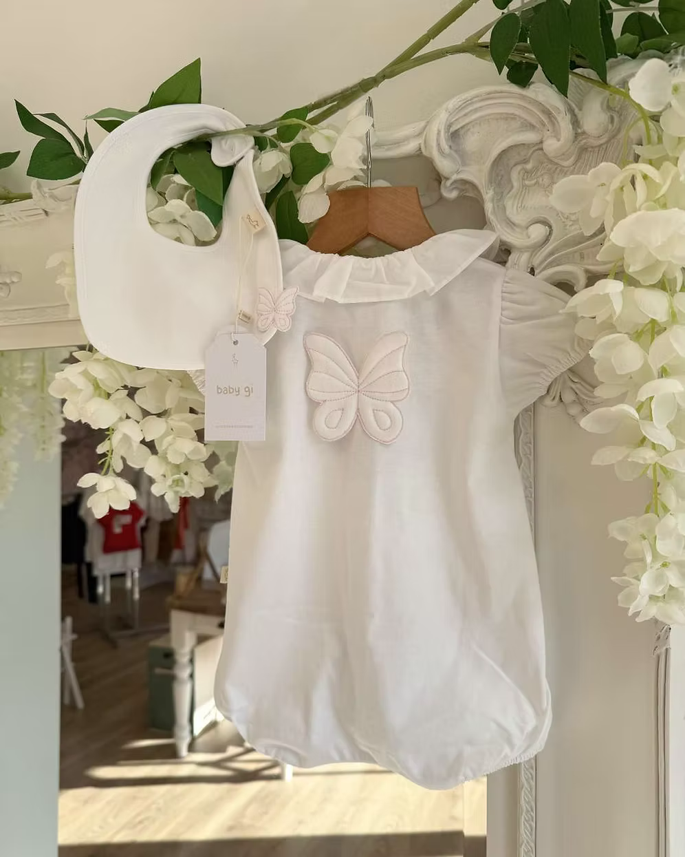 Baby Gi Butterfly Back Romper featuring a white bubble design, oversized butterfly back detail, pink embroidered trims and a frill collar. Alongside the matching bib.