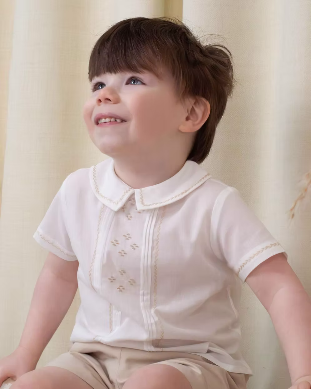 Sarah Louise x Little Lambs Heritage Boys Short Set featuring an ivory shirt with traditional detailing and tailored beige shorts.