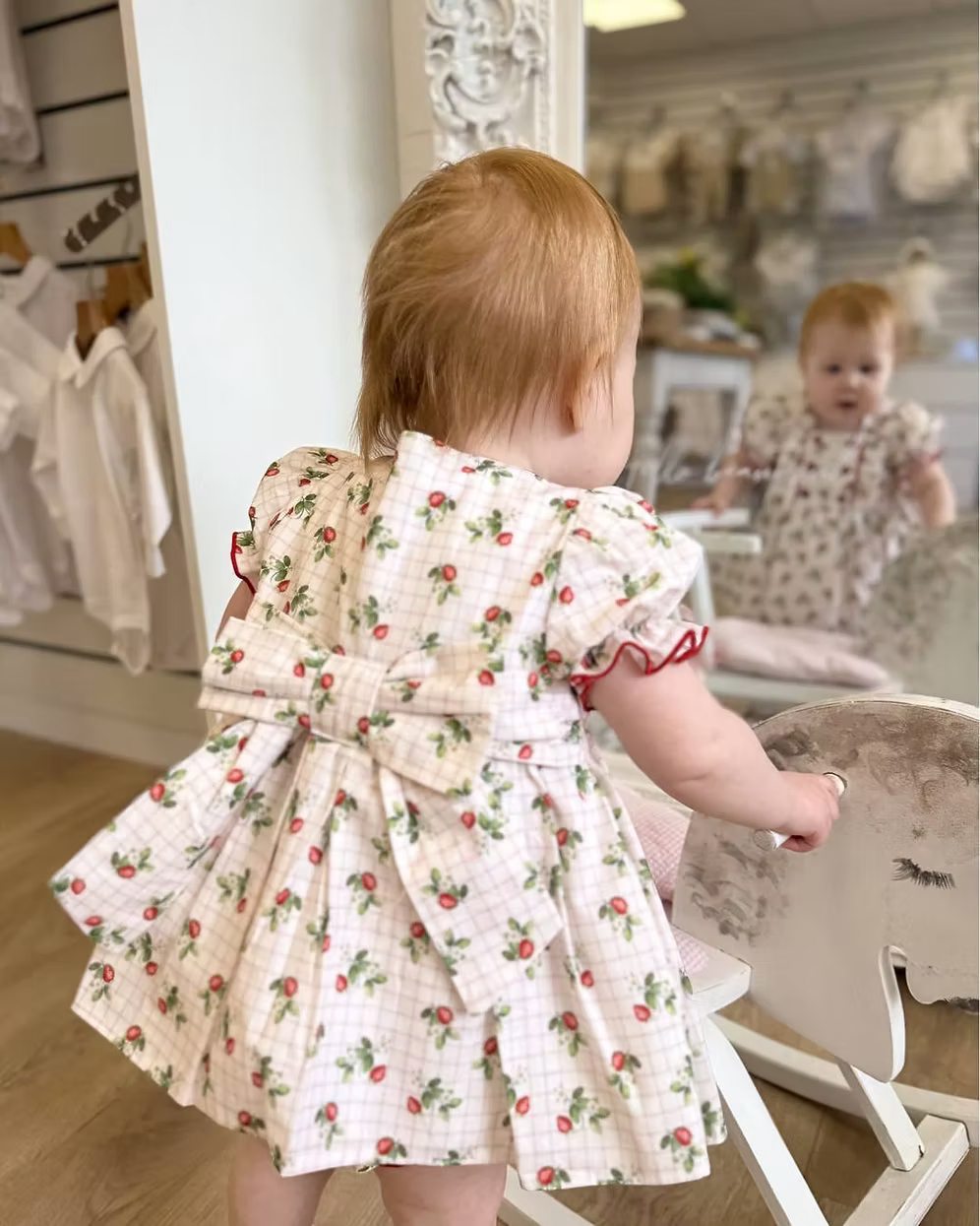 Off-white and pink check baby dress with strawberry print, frill chest detail, puff sleeves, red stitch trims, matching pants, and bow back fastening.